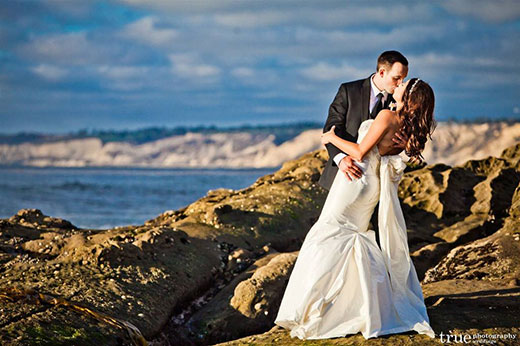 A bride and groom kissing on the rocks